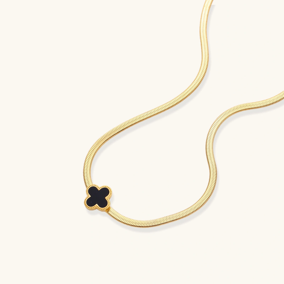 Dainty 18K gold-plated herringbone chain necklace with black enamel quatrefoil clover pendant on white background