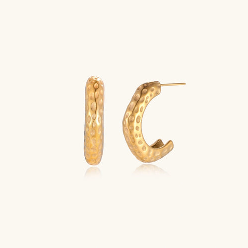 Gold-toned hoop earrings with hammered dimpled texture and post closure on cream background