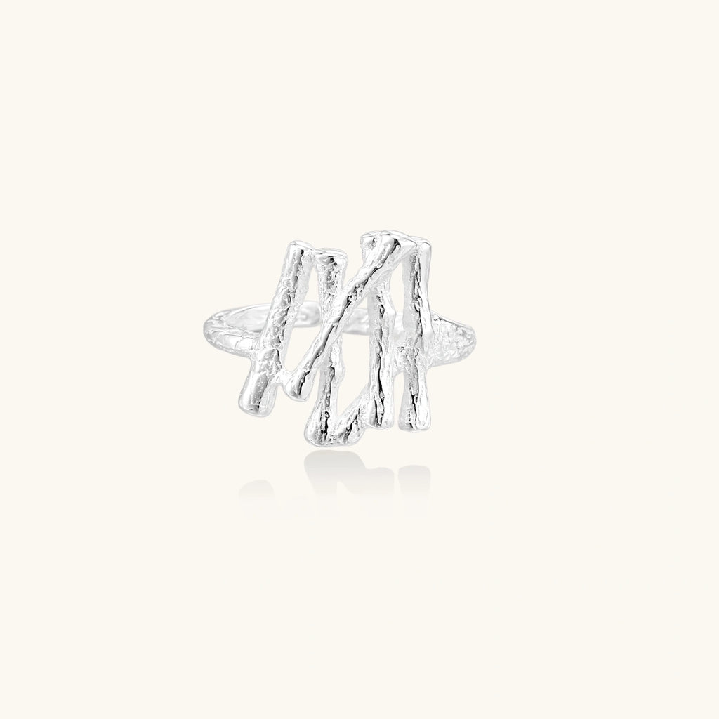 Sculptural sterling silver ring with organic branch design and textured surfaces on cream background